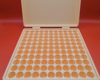 May include: A beige plastic storage case with a grid of 100 round compartments. The case is open and the compartments are empty.