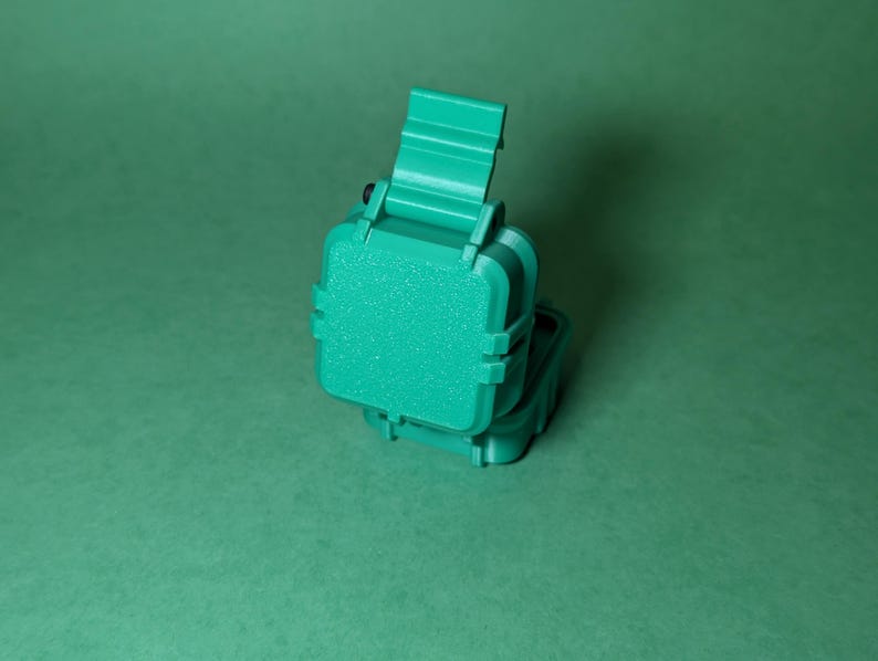 Puede incluir: Una caja de pl&aacute;stico verde azulado con una tapa con bisagras. La caja est&aacute; cerrada y la tapa est&aacute; ligeramente entreabierta. La caja es texturizada y tiene un acabado mate.