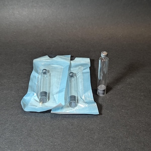 May include: Three clear glass vials with silver caps, packaged in a blue paper wrapper. The vials are arranged in a row, with the caps facing the viewer.