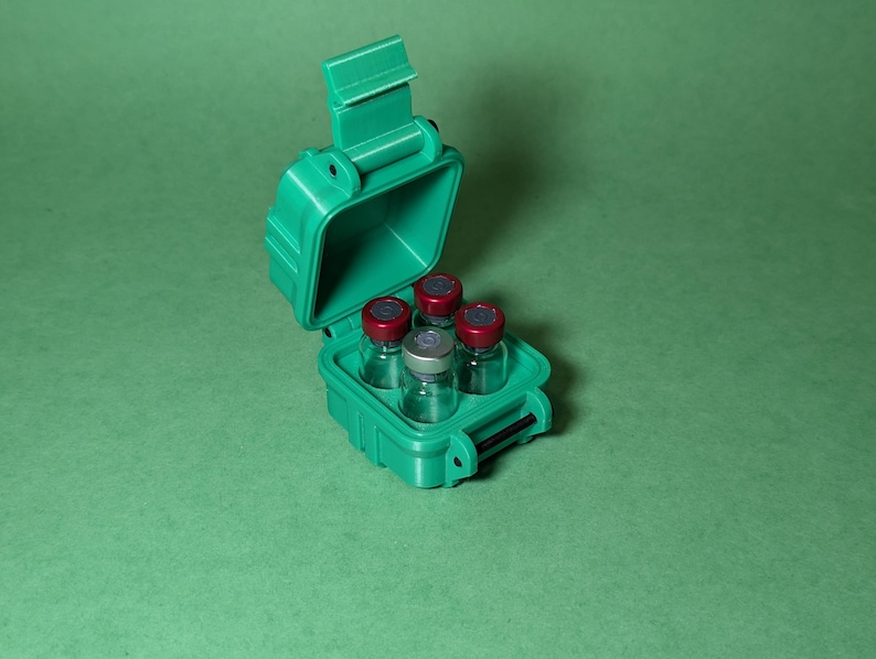 Puede incluir: Una caja de pl&aacute;stico verde con una tapa con bisagras, abierta para revelar seis peque&ntilde;os viales de vidrio con tapas rojas. Los viales est&aacute;n dispuestos en una cuadr&iacute;cula dentro de la caja.