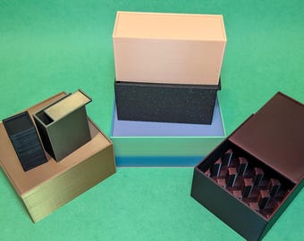 May include: Four boxes stacked on top of each other. The top box is light pink, the second box is black with a speckled texture, the third box is light blue, and the bottom box is green and blue with a striped pattern. The boxes are made of cardboard and have a variety of textures.