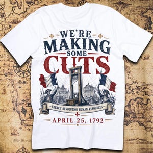 May include: A white t-shirt featuring a graphic print with the text WE'RE MAKING SOME CUTS, FRENCH REVOLUTION HUMAN RESOURCES, and APRIL 25, 1792. The design includes a guillotine, two French flags, and figures in historical attire.