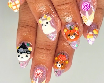 May include: Close-up of a hand with several Halloween-themed nail designs. The nails are painted in a light purple color and feature various 3D decorations, including a ghost, a witch, a bear with a pumpkin, and a lollipop.