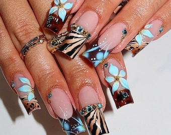 May include: Long square-shaped artificial nails featuring a French manicure base with a mix of brown tortoiseshell patterns, black zebra stripes, and three-dimensional light blue floral accents. The design is embellished with small blue rhinestones.