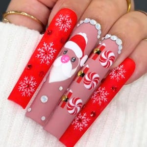 Könnte beinhalten: Lange, rosafarbene und rote künstliche Nägel mit Weihnachtsmotiven. Die Nägel zeigen Schneeflocken, Zuckerstangen und ein Weihnachtsmann-Motiv.