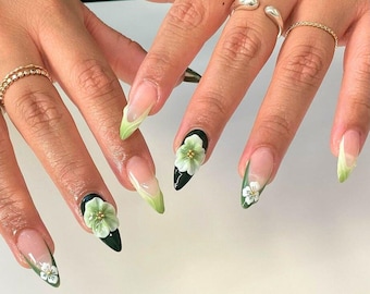 Op de afbeelding: Close-up van handen met lange, amandelvormige nagels. De nagels zijn geverfd met een lichtgroene gradiënt en hebben 3D witte bloemen erop.