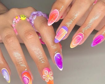 Op de afbeelding: Close-up van een hand met lange, amandelvormige nagels die zijn geverfd met verschillende kleurrijke ontwerpen. De nagels hebben een mix van abstracte patronen, bloemen en geometrische vormen in tinten roze, oranje, paars en geel.