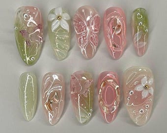 Op de afbeelding: Tien lange, ovale kunstnagels met een lichtgroene en roze basis. Elke nagel is versierd met een ander ontwerp, waaronder vlinders, bloemen en swirls.