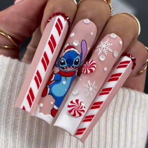 May include: Long, pink and white acrylic nails with a candy cane design. One nail features a cartoon Stitch character wearing a Santa hat. The nails are decorated with white snowflakes and red and white candy cane swirls.