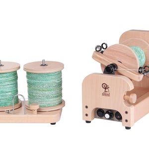 May include: A wooden spinning wheel with two spools of green yarn. The spinning wheel has a foot pedal and a control knob. The spools are on a separate wooden base.