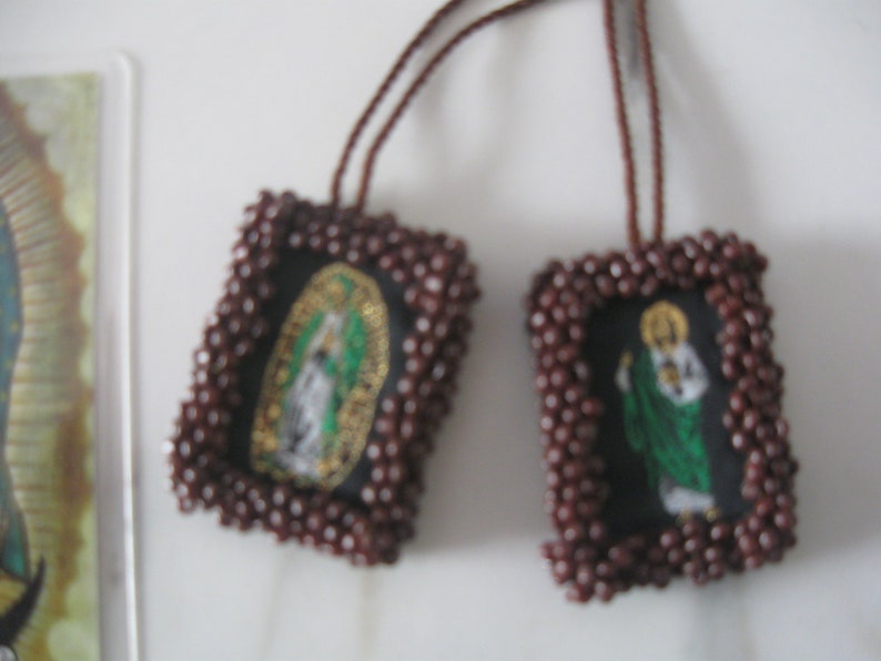 May include: Two brown beaded religious charms with images of saints. The charms are attached to brown cords.
