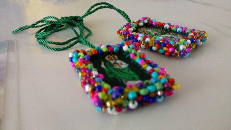 May include: Two rectangular pendants with colorful beaded frames and green cords. The pendants feature religious imagery. The beads are in various colors, including red, blue, yellow, and green. The cords are a bright green color.