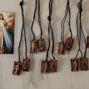 Könnte beinhalten: Eine Sammlung religiöser Anhänger mit braunen Kordeln und rechteckigen, bestickten Anhängern. Jeder Anhänger zeigt ein religiöses Bild mit blauen, roten und goldenen Akzenten. Eine religiöse Karte mit einem Bild von Jesus ist ebenfalls zu sehen.