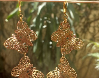 May include: A pair of gold-tone dangle earrings featuring three layered butterfly charms. Each butterfly charm has a delicate, intricate design.