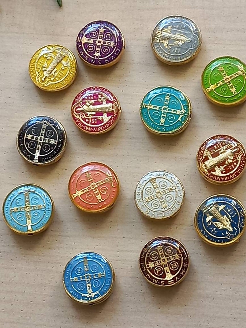 Puede incluir: Una colecci&oacute;n de 14 medallones redondos con borde dorado y dise&ntilde;os de esmalte de varios colores. Cada medall&oacute;n presenta una cruz con diferentes s&iacute;mbolos y texto, incluyendo las palabras "S-M-V-R-S-N-S" y "P-L-U-B-N-R-D-S".