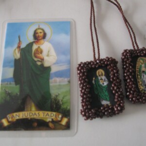 May include: A brown beaded prayer card with a picture of Saint Jude Thaddeus. The card is attached to a brown cord and has the text "San Judas Tadeo" on the bottom.