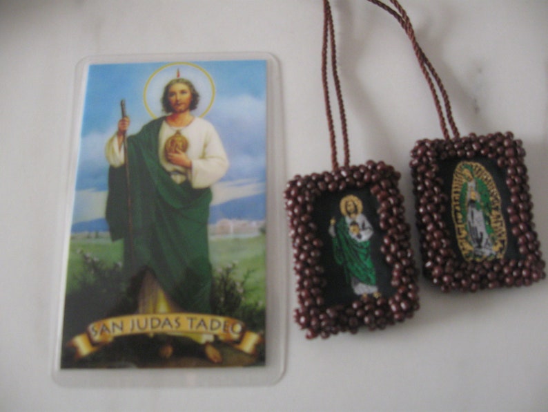 May include: A brown beaded prayer card with a picture of Saint Jude Thaddeus. The card is attached to a brown cord and has the text "San Judas Tadeo" on the bottom.