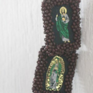 May include: Two small framed images with religious figures. The frames are made of brown beads and the images are of Jesus and the Virgin Mary.