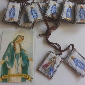 以下が含まれることがあります： 聖母マリアの画像が描かれた小さな長方形の布製チャームの集まり。チャームは茶色の紐に通されています。チャームは白地に青と金のアクセントが施されています。チャームの1つには「VIRGEN MILAGROSA」という文字が印刷されています。