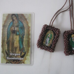 May include: Two brown beaded religious medallions with images of Virgin Mary and a saint, hanging from a brown cord. A card with the image of Virgin Mary and the text "Virgen Guadalupe" is in the background.