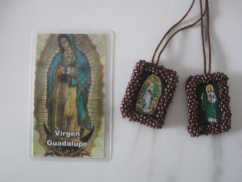 May include: Two brown beaded religious medallions with images of Virgin Mary and a saint, hanging from a brown cord. A card with the image of Virgin Mary and the text "Virgen Guadalupe" is in the background.