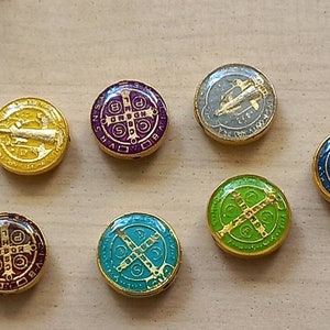 Puede incluir: Siete amuletos redondos de metal de color dorado con dise&ntilde;os de esmalte de diferentes colores. Los amuletos presentan s&iacute;mbolos religiosos y texto.