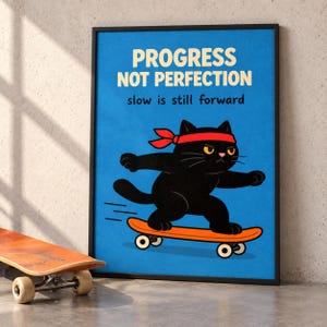 Könnte beinhalten: Ein gerahmtes Poster mit blauem Hintergrund zeigt eine schwarze Katze mit rotem Stirnband auf einem orangefarbenen Skateboard. Der Text lautet PROGRESS NOT PERFECTION und slow is still forward in schwarzer und weißer Schrift.