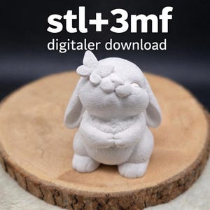 May include: A white bunny figurine with a butterfly on its head, placed on a wooden slice. The bunny has closed eyes and clasped hands. The text "stl+3mf digitaler download" is at the top.