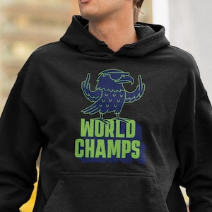May include: Black hooded sweatshirt with a blue and green graphic of a bird wearing sunglasses and the words "WORLD CHAMPS". The sweatshirt has a front pocket and is worn with blue jeans. The image is taken outdoors.