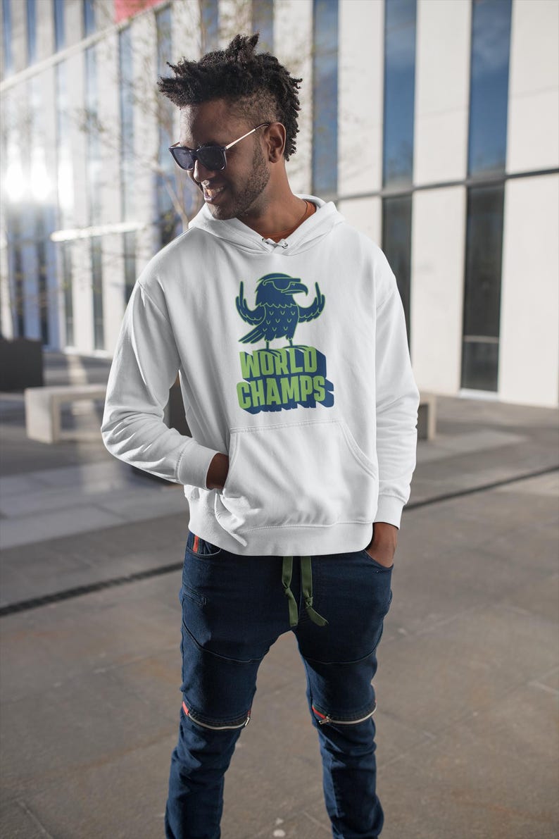 May include: White hooded sweatshirt with a graphic of a blue eagle wearing sunglasses and the words "WORLD CHAMPS" in green and blue. The sweatshirt has a front pocket and is being worn with blue jeans.