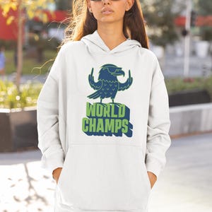 May include: White hoodie with a blue and green graphic of a bird with sunglasses and the words "WORLD CHAMPS". The hoodie has a front pocket and a hood. The person is wearing sunglasses.