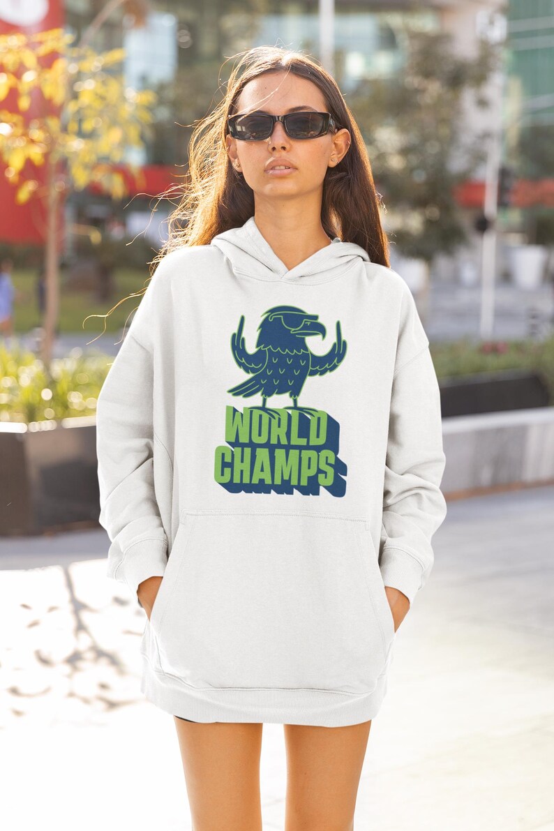 May include: White hoodie with a blue and green graphic of a bird with sunglasses and the words "WORLD CHAMPS". The hoodie has a front pocket and a hood. The person is wearing sunglasses.