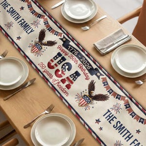 Puede incluir: Camino de mesa beige con diseños patrióticos en rojo, blanco y azul. Presenta el texto "USA", "Happy 250th Birthday" y "The Smith Family". El camino de mesa está decorado con águilas y estrellas.