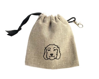Puede incluir: Una pequeña bolsa de lino beige con cordón de ajuste, cordón negro y clip plateado. La bolsa tiene una imagen bordada en negro de una cabeza de perro en la parte delantera.