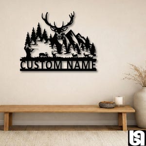 May include: Black metal wall art featuring a deer with large antlers, set against a mountain and forest scene. The design includes the text "CUSTOM NAME" at the bottom, perfect for personalized home decor.