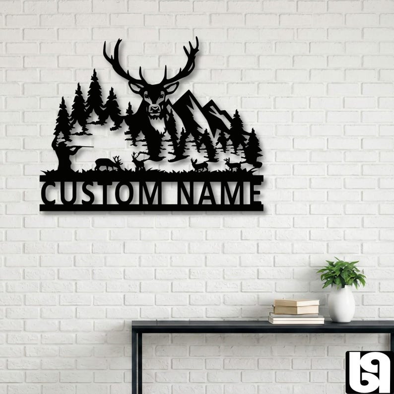 May include: Black metal wall art featuring a deer with large antlers, mountains, and trees. The silhouette includes a hunter and deer. The text "CUSTOM NAME" is at the bottom. The artwork is mounted on a white brick wall.