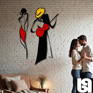 May include: A couple dances in front of a white brick wall with a black and red silhouette of a musician playing a guitar. The musician is wearing a yellow hat.