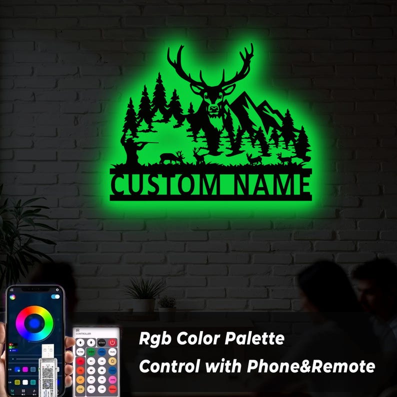 May include: A black metal wall art piece featuring a deer, trees, mountains, and a hunter silhouette, illuminated with a green glow. The text "CUSTOM NAME" is displayed below the design. The image also shows a phone and remote control for color adjustments.
