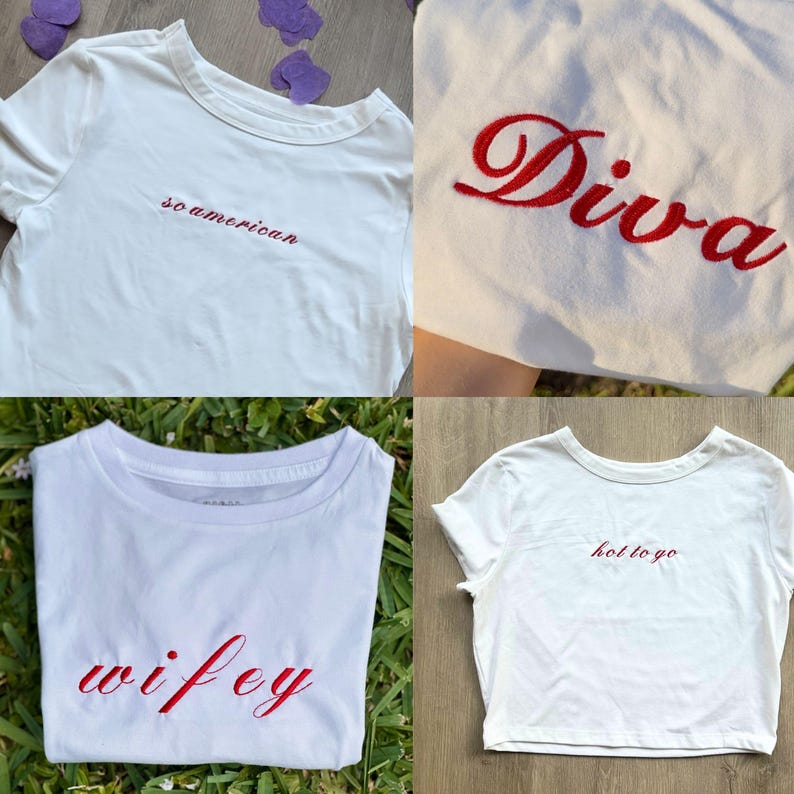 Op de afbeelding: Vier witte t-shirts met rood geborduurde tekst. De shirts tonen de woorden "so american", "Diva", "wifey" en "hot to go". De shirts worden gepresenteerd op een wit oppervlak en op groen gras.