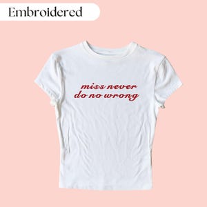 May include: White t-shirt with red embroidered text that reads "miss never do no wrong".
