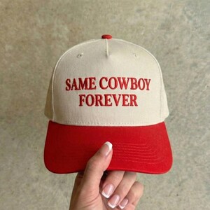 Puede incluir: Gorra de b&eacute;isbol con corona color crema y visera roja. Las palabras "SAME COWBOY FOREVER" est&aacute;n bordadas en rojo en la parte delantera. La gorra tiene un bot&oacute;n rojo en la parte superior.