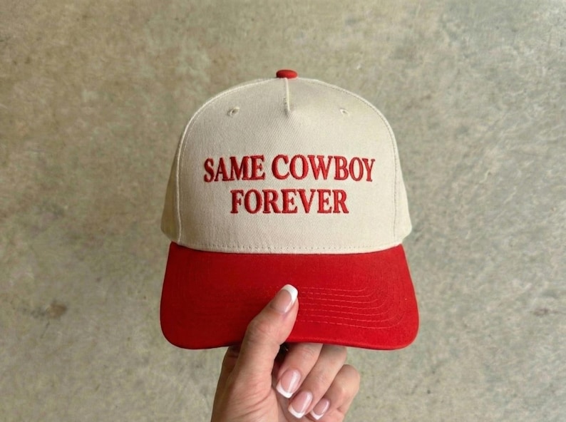 Puede incluir: Gorra de b&eacute;isbol con corona color crema y visera roja. Las palabras "SAME COWBOY FOREVER" est&aacute;n bordadas en rojo en la parte delantera. La gorra tiene un bot&oacute;n rojo en la parte superior.