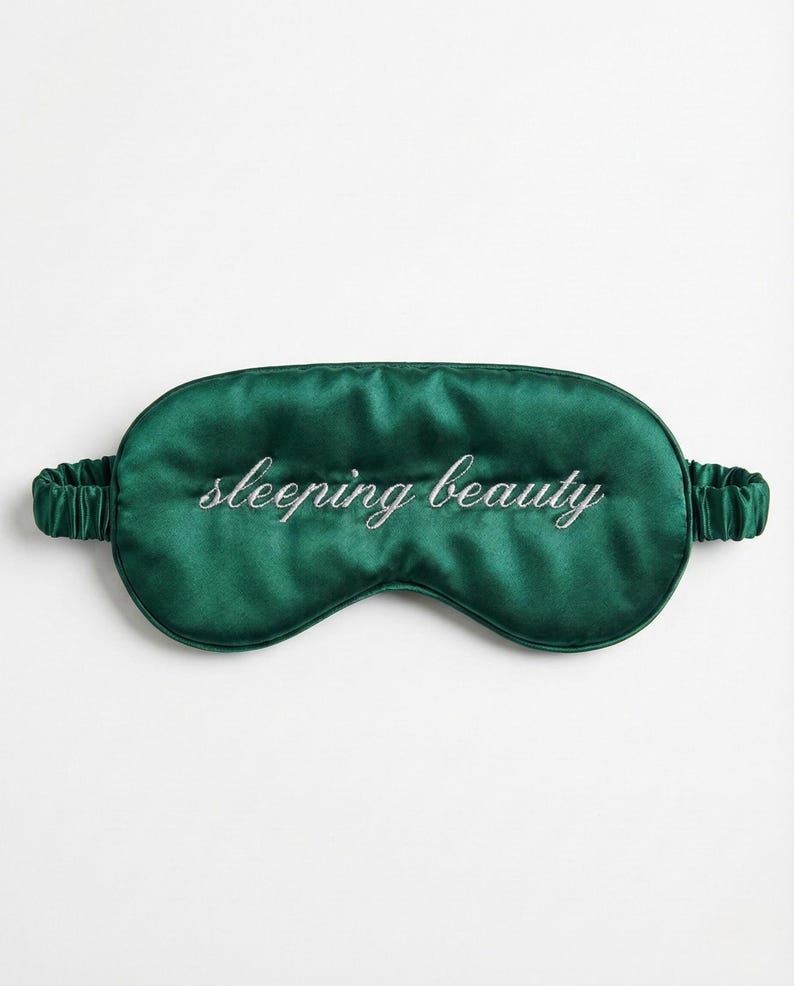 Puede incluir: M&aacute;scara para dormir de sat&eacute;n verde esmeralda con la inscripci&oacute;n bordada "sleeping beauty" en letra cursiva. La m&aacute;scara tiene una banda el&aacute;stica para un ajuste c&oacute;modo. Un accesorio de lujo para un sue&ntilde;o reparador.