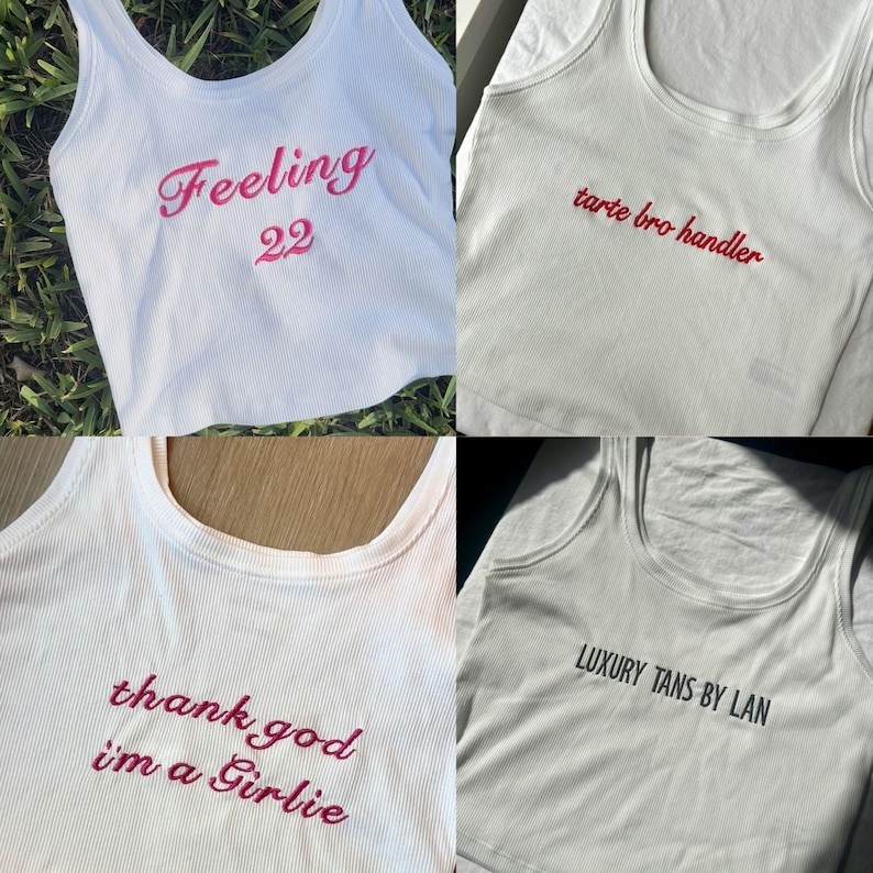 May include: Four white ribbed tank tops with embroidered text in pink and black. The phrases include "Feeling 22", "tarte bro handler", "thank god i'm a Girlie", and "LUXURY TANS BY LAN".
