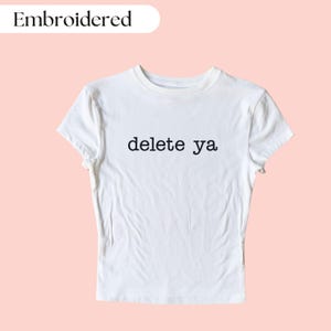 Op de afbeelding: Wit gecropped T-shirt met de tekst "delete ya" geborduurd in zwart.