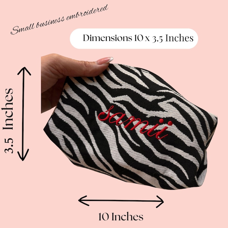 May include: A black and white zebra print cosmetic bag with the name "Sami" embroidered in red. The bag measures 10 x 3.5 inches. The text "Small business embroidered" is above the bag.