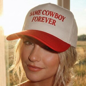 Puede incluir: Gorra de b&eacute;isbol con corona blanca y visera roja. El texto "SAME COWBOY FOREVER" est&aacute; bordado en rojo en la parte delantera. La gorra la lleva una persona con cabello rubio.