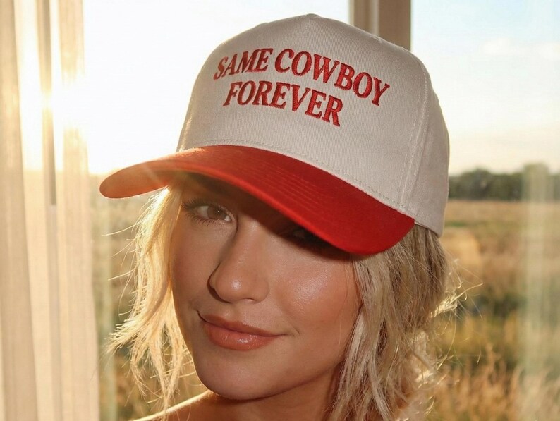 Puede incluir: Gorra de b&eacute;isbol con corona blanca y visera roja. El texto "SAME COWBOY FOREVER" est&aacute; bordado en rojo en la parte delantera. La gorra la lleva una persona con cabello rubio.