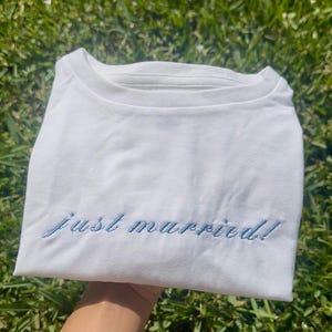 May include: White t-shirt with blue embroidery that says "just married!"