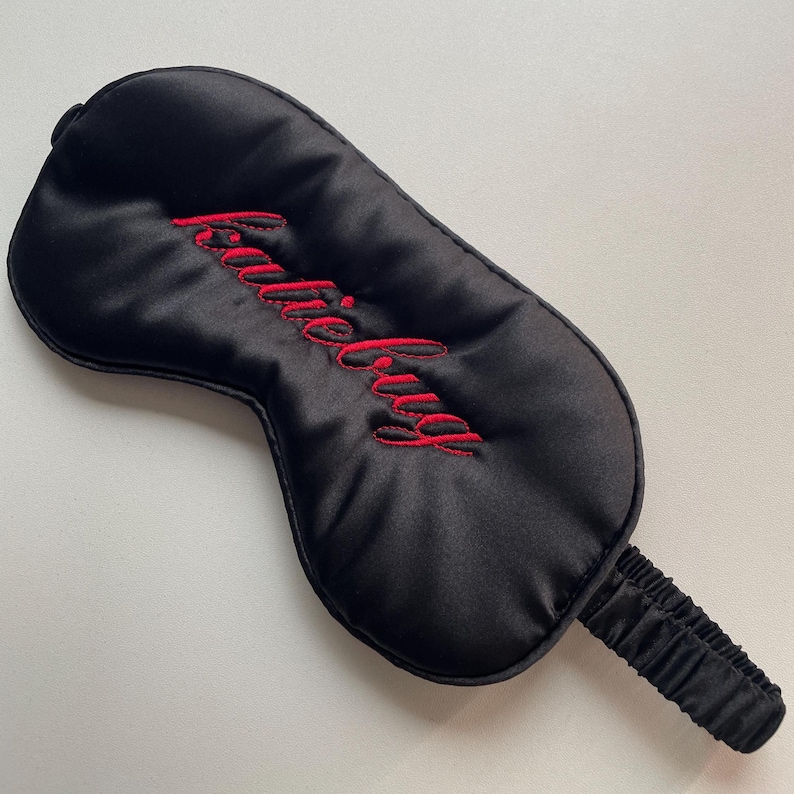 Puede incluir: M&aacute;scara para dormir de sat&eacute;n negro con el texto bordado "Katie Bug" en escritura roja. La m&aacute;scara tiene una forma contorneada y una banda el&aacute;stica para un ajuste c&oacute;modo. Un accesorio para dormir para un sue&ntilde;o reparador.
